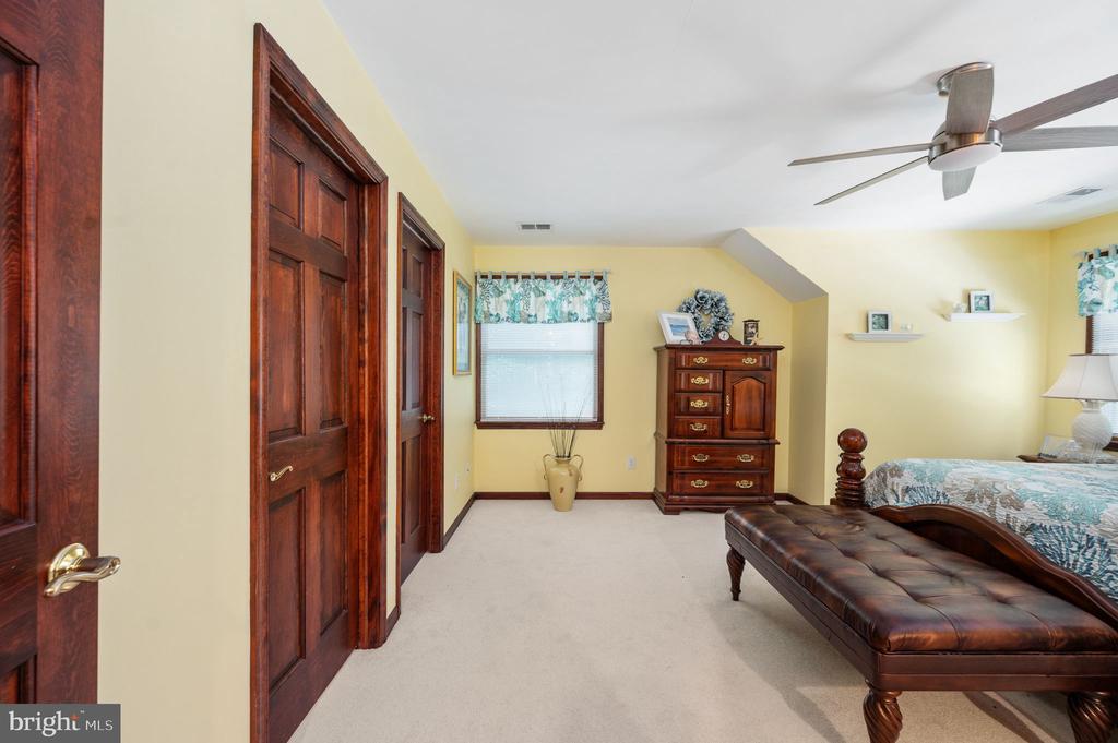 Furnished bedroom with dark wood doors and dresser, a ceiling fan, and a leather bench.