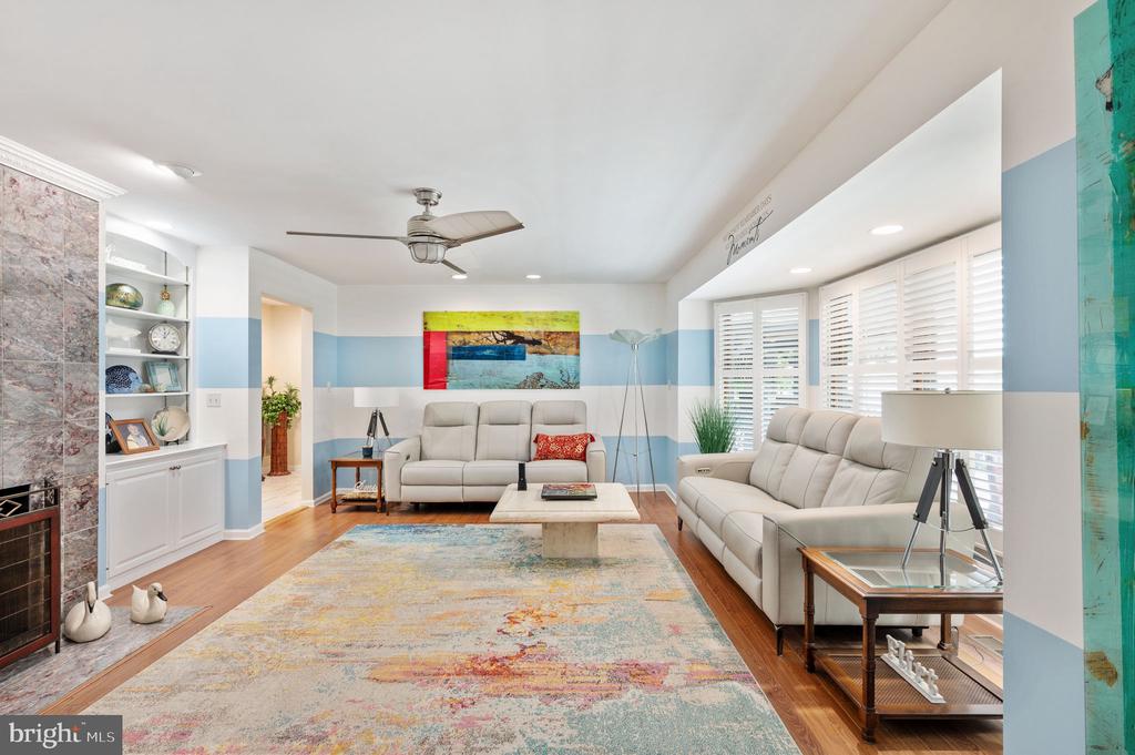 Living room with two light sofas, a stone fireplace, built-in shelving, and white plantation shutters.
