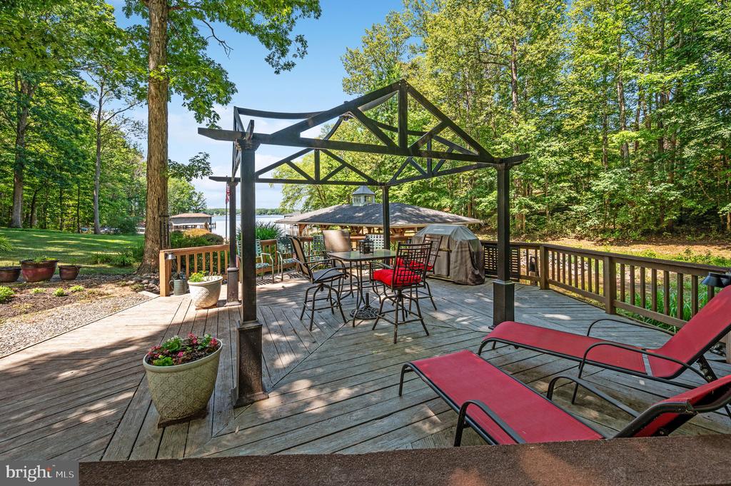 Wooden deck with a black pergola, patio seating, and a glimpse of the lake beyond.