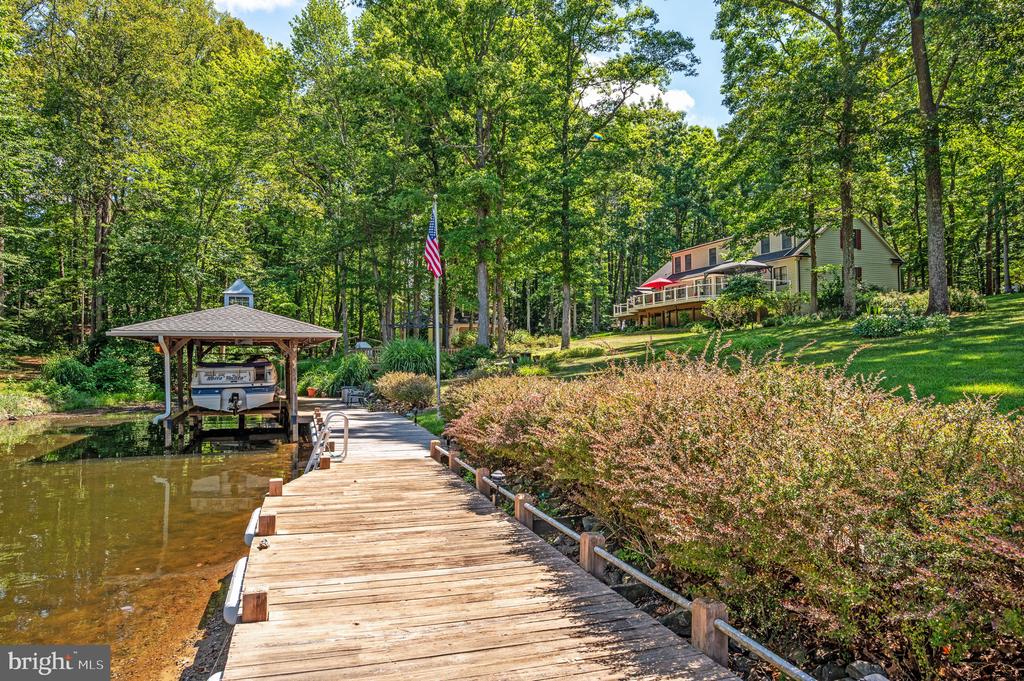 Wooded waterfront home above a long wooden dock and covered boat slip.