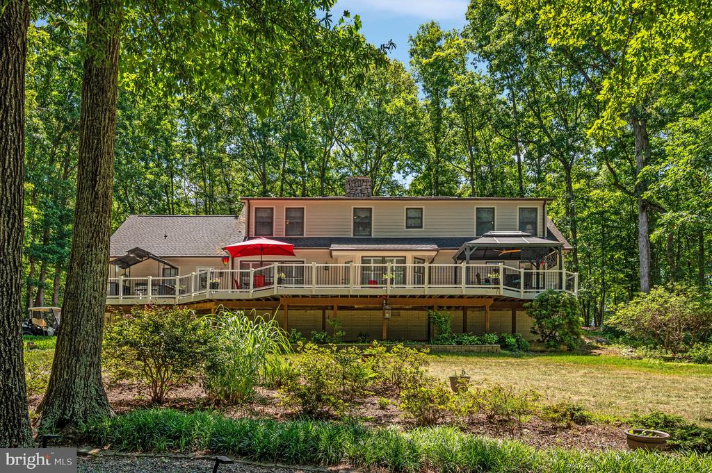 Two-story home with a long elevated deck and red umbrella, surrounded by mature trees.