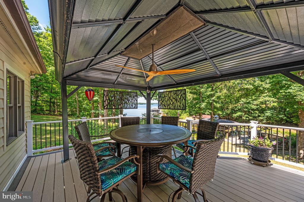 Covered deck with outdoor dining set and ceiling fan overlooking trees and a lake
