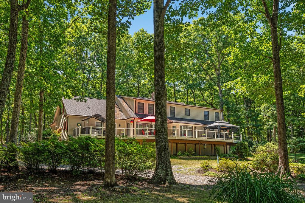 Two-story home nestled among trees, with a raised deck and patio umbrellas.