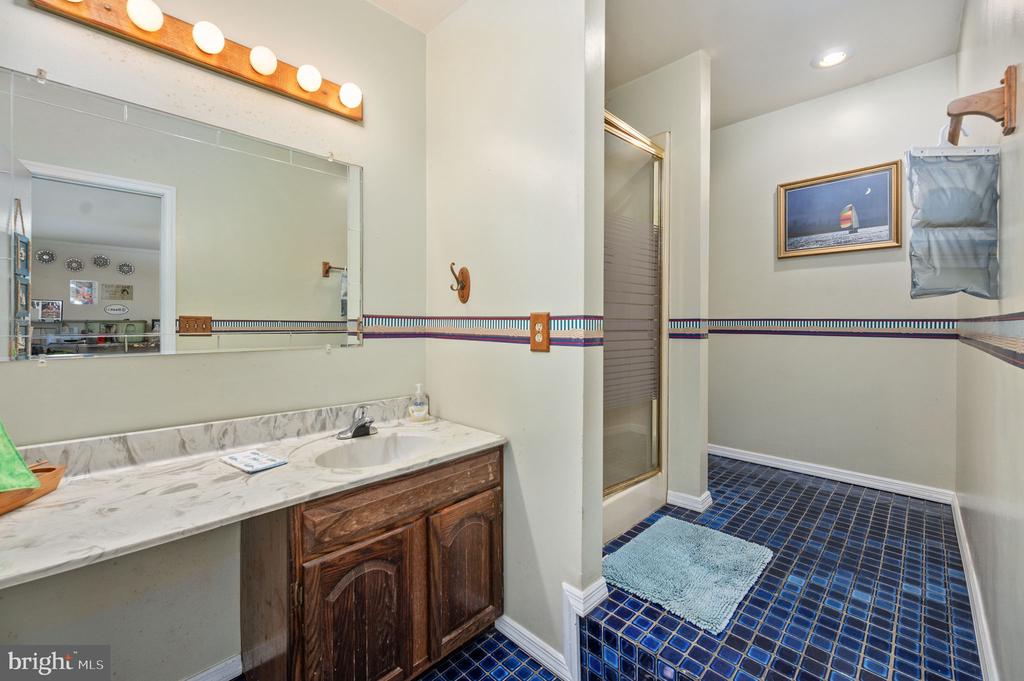 Bathroom with a marble-look vanity, dark wood cabinets, glass shower, and blue tile floor.