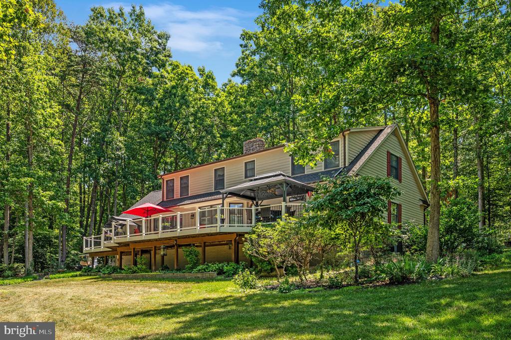Two-story wooded home with a raised deck, red umbrella, and covered seating area.
