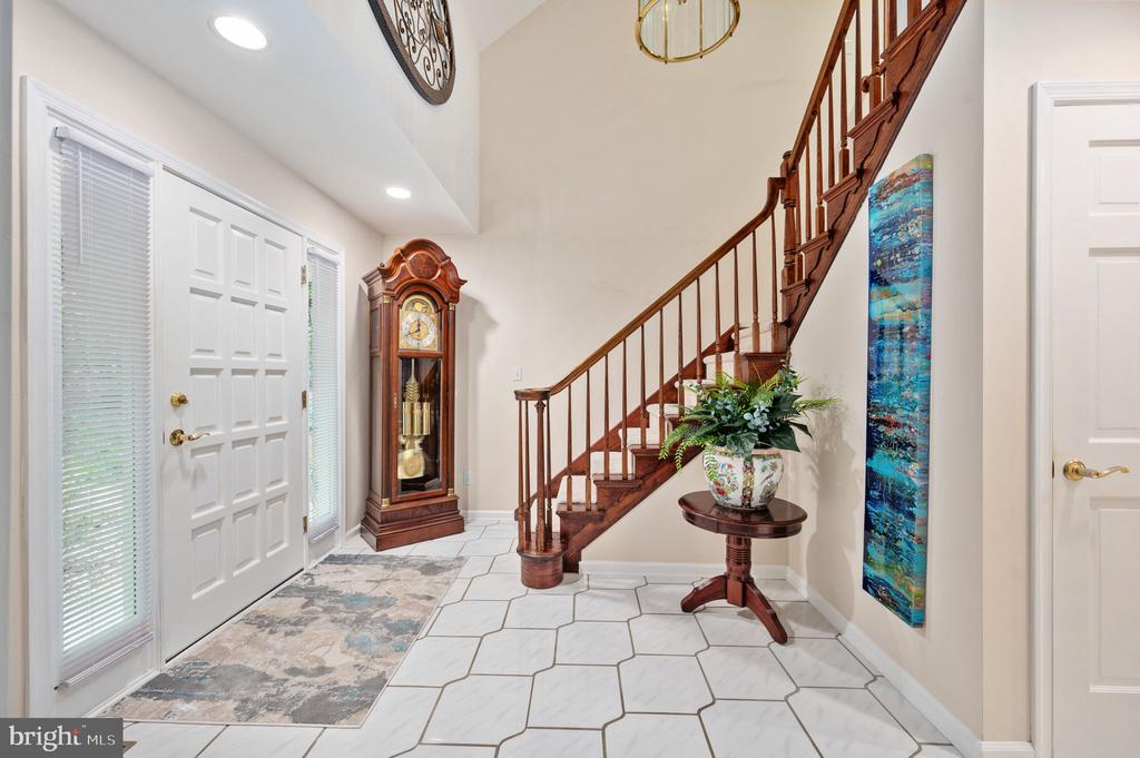 Entry foyer with a wooden staircase, patterned tile floor, and grandfather clock.
