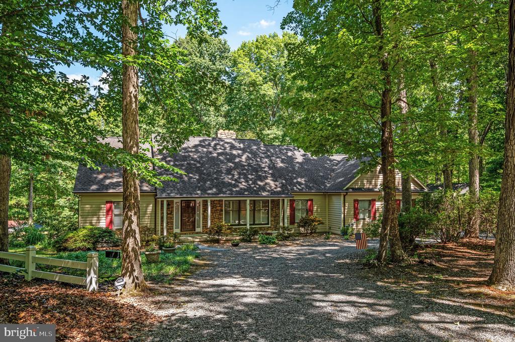 Tree-shaded home with a stone-accented facade, red shutters, and a wide gravel driveway.
