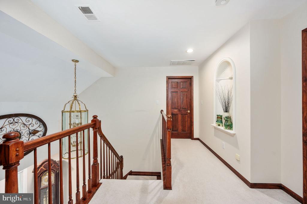Upstairs hallway with a dark wood stair railing, cream carpet, and an arched display niche.