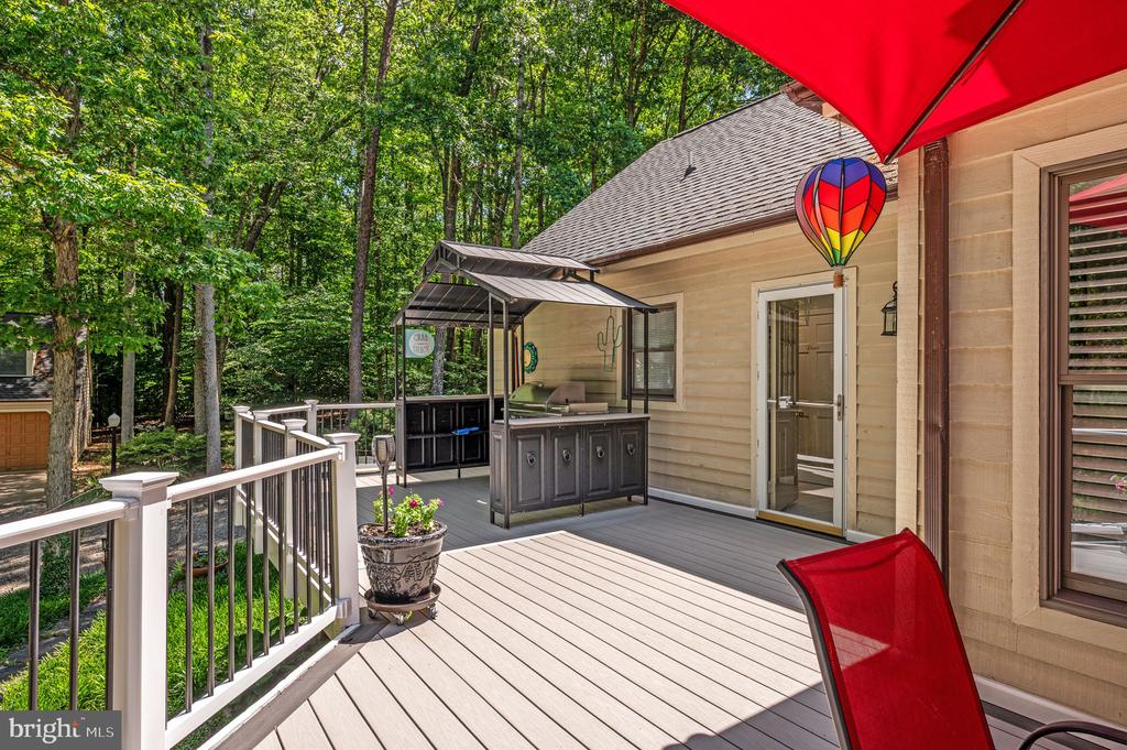 Wooded home deck with an outdoor kitchen, white railings, and a bright red umbrella.