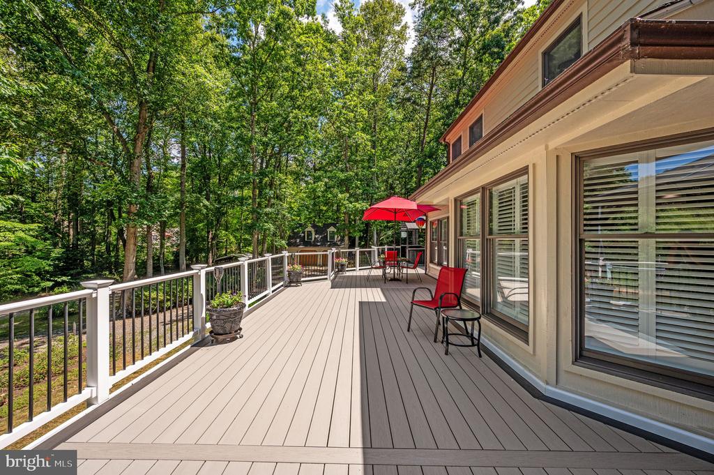 Spacious deck with red patio chairs and umbrella, bordered by white railings and dense trees.