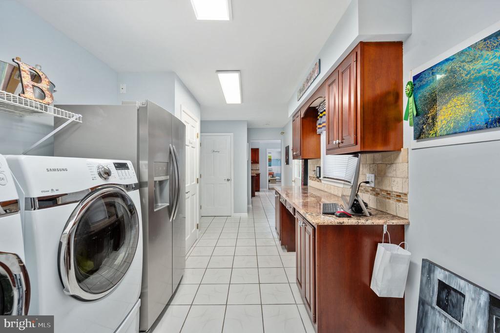 Laundry room with a front-loading washer and dryer, stainless-steel refrigerator, and long wood cabinets.