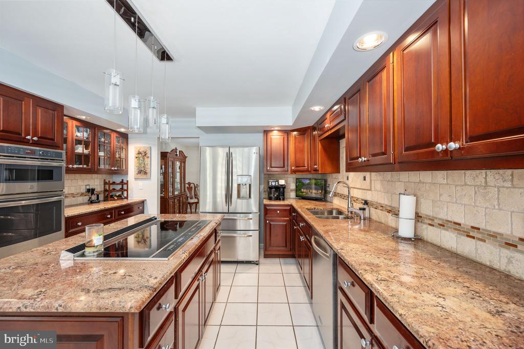 Kitchen with dark wood cabinetry, granite counters, stainless steel appliances, and a central cooktop island.