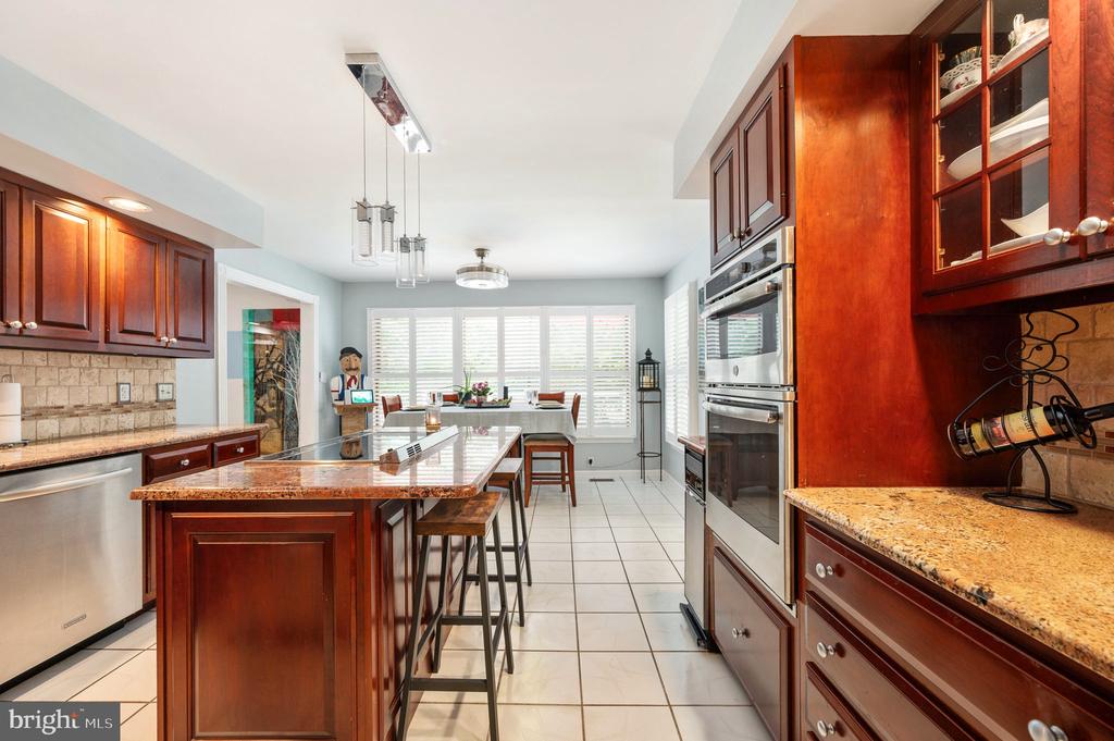 Kitchen with cherry cabinets, granite island, stainless steel appliances and a dining area by shuttered windows.