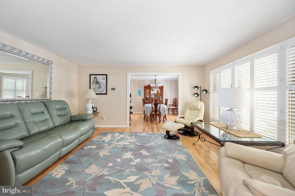 Living room with a green leather sofa, cream recliner, and blue floral rug beside shuttered windows.