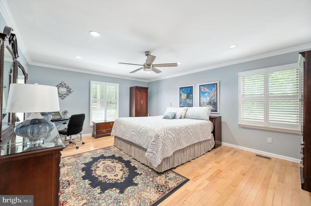 Bedroom with a large bed, plantation shutters, ceiling fan, and patterned rug.