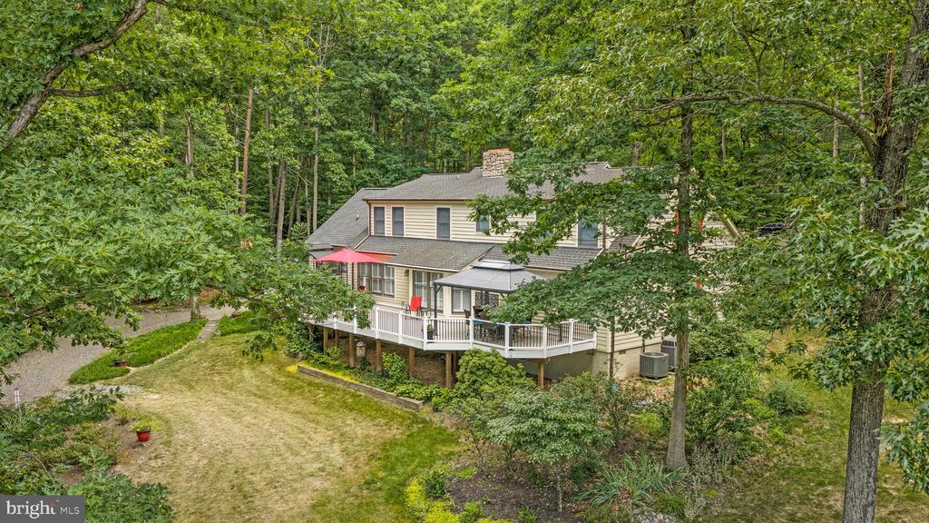 Wooded two-story home with a white wraparound deck and red patio umbrella.