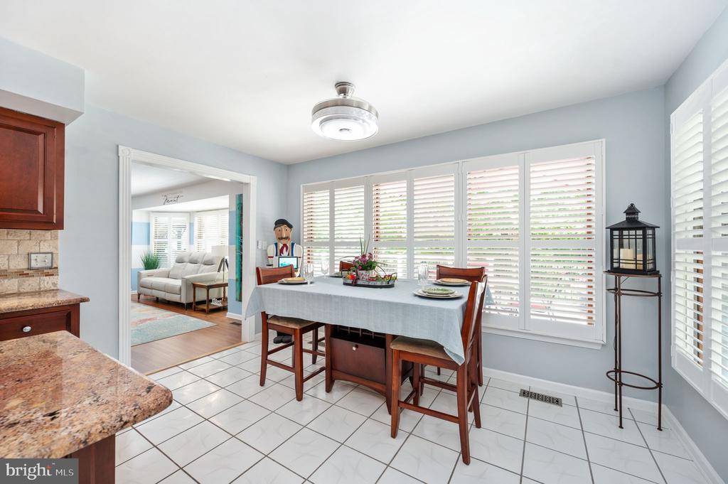 Dining area with a set wooden table beside broad windows with white shutters.