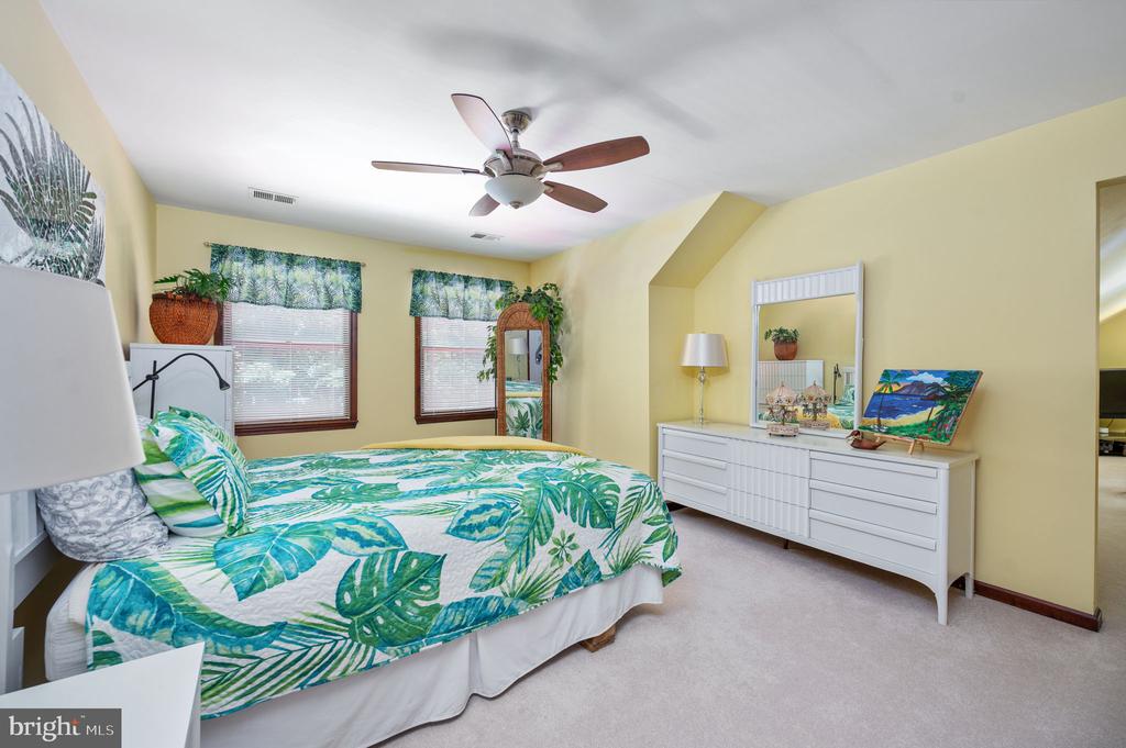 Bedroom with tropical leaf-print bedding, two windows, a ceiling fan, and a white dresser.