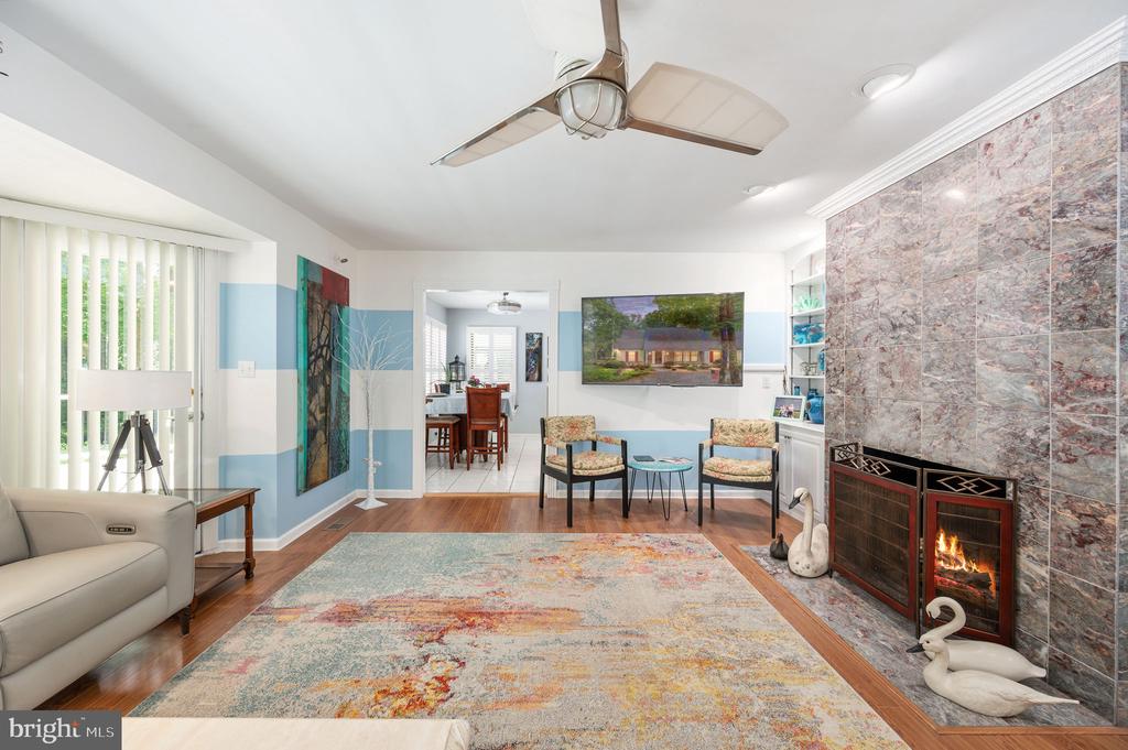 Living room with a stone fireplace, ceiling fan, colorful rug, and adjoining dining area.
