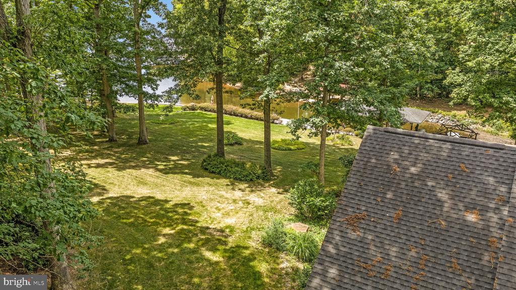Elevated view of a wooded lawn beside the water, with a roof in the foreground.