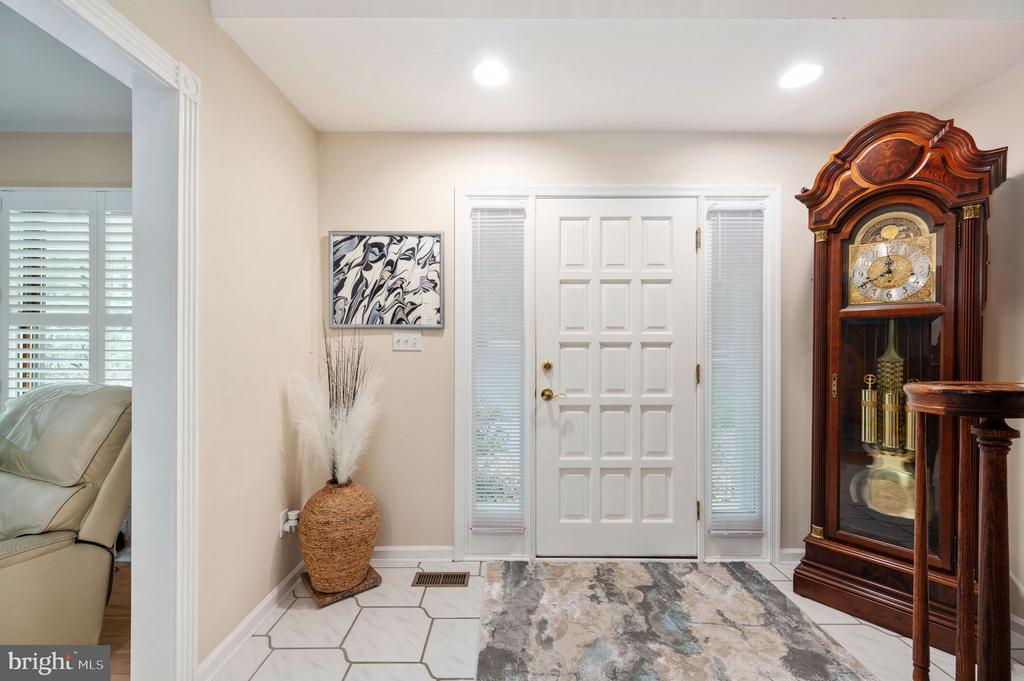Entry foyer with a white paneled door, geometric tile floor, patterned runner, and wooden grandfather clock.