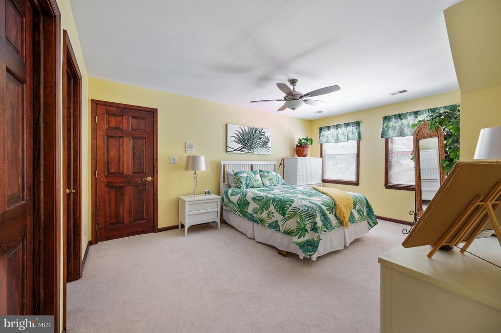 Bedroom with tropical-print bedding, dark wood doors, and two curtained windows.