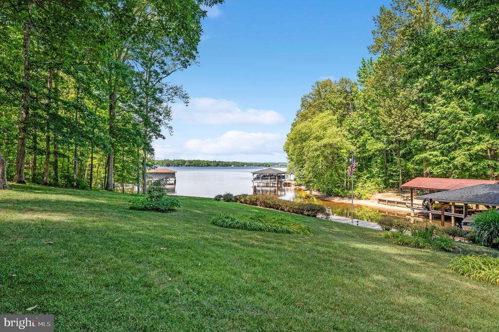Grassy lawn slopes toward a lake with covered docks, framed by mature green trees.