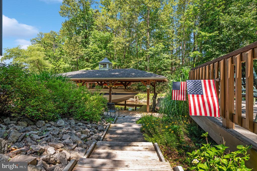 Covered boat dock and wooden walkway beside a wooded shoreline, with two American flags on the deck.