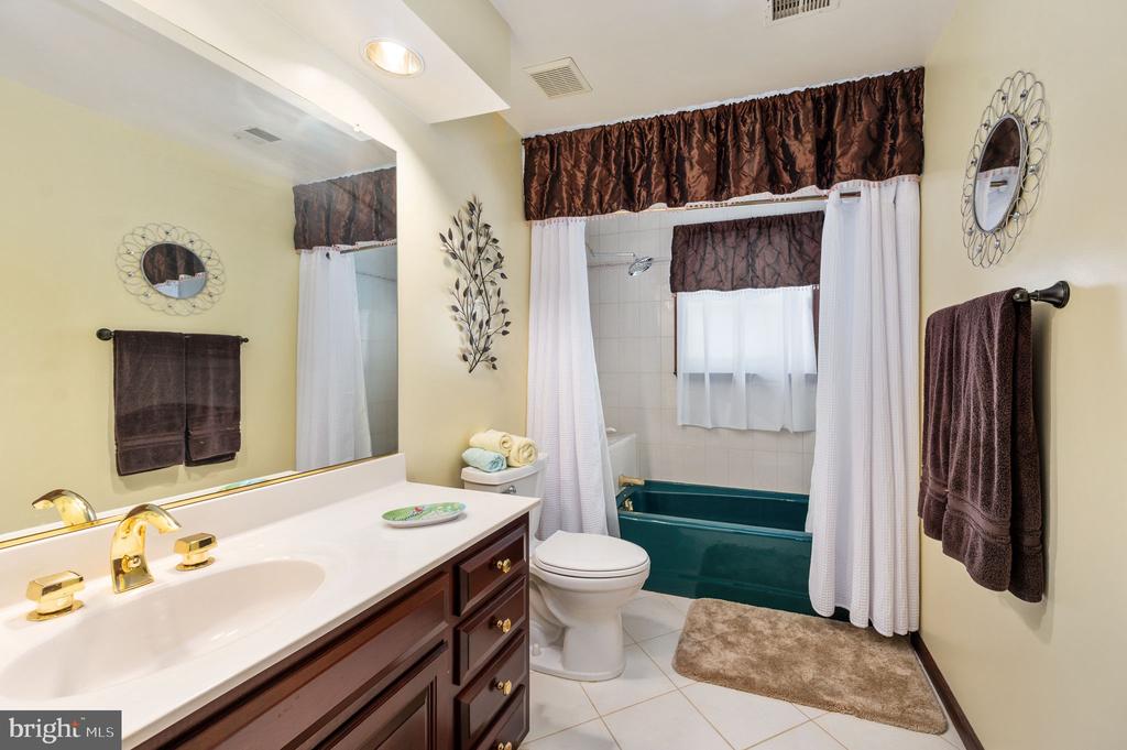 Bathroom with a long wood vanity, large mirror, and teal bathtub behind white curtains.