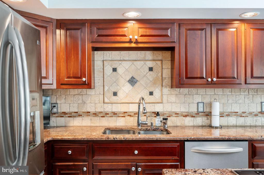 Kitchen with cherry cabinets, a decorative tile backsplash, granite counters, and a stainless-steel dishwasher.