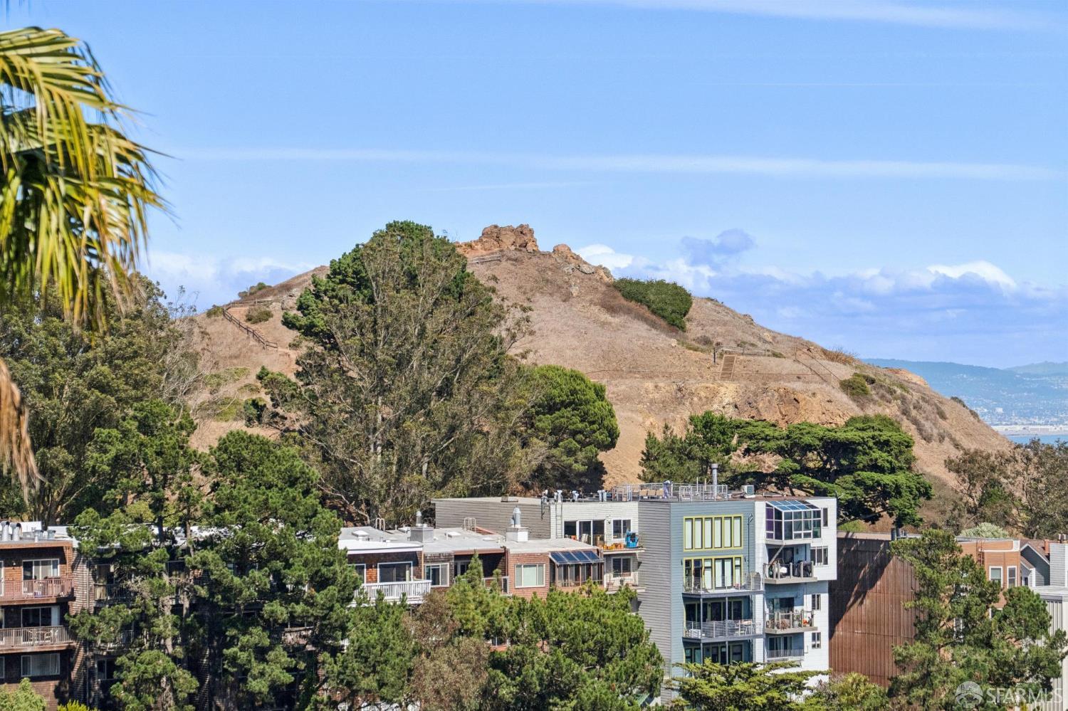 Residential buildings below a rocky hillside, with water visible in the distance.