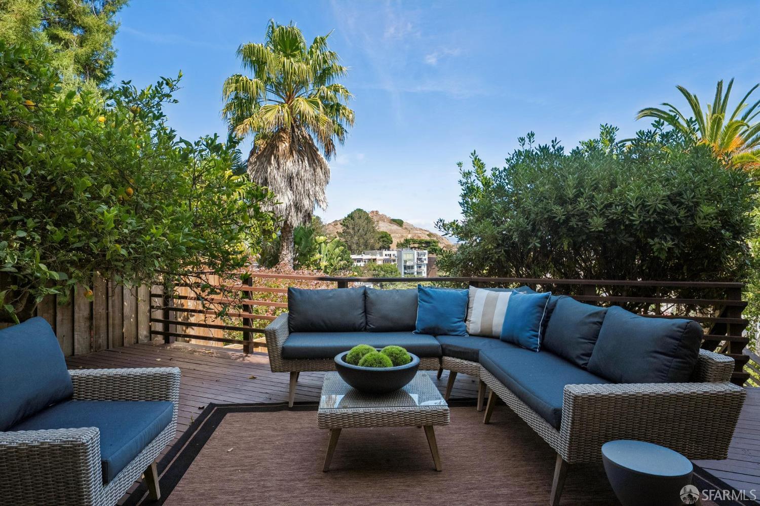 Outdoor deck with blue-cushioned wicker seating, palm trees, and a hillside view.