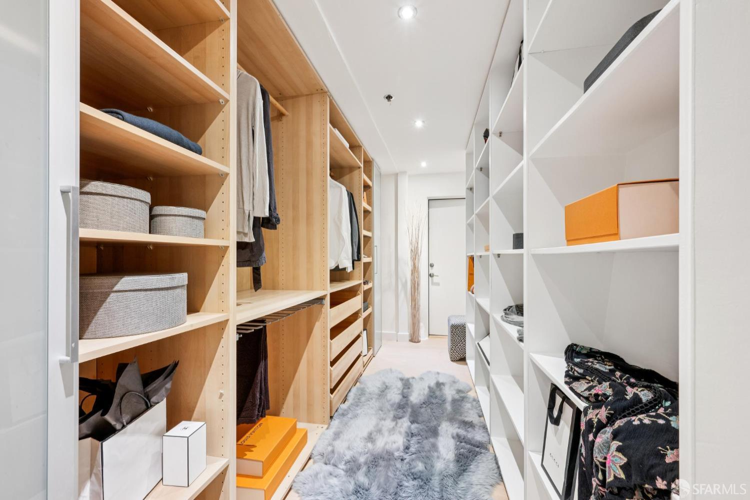 Walk-in closet with light wood shelving, hanging clothes, and a gray shag rug.
