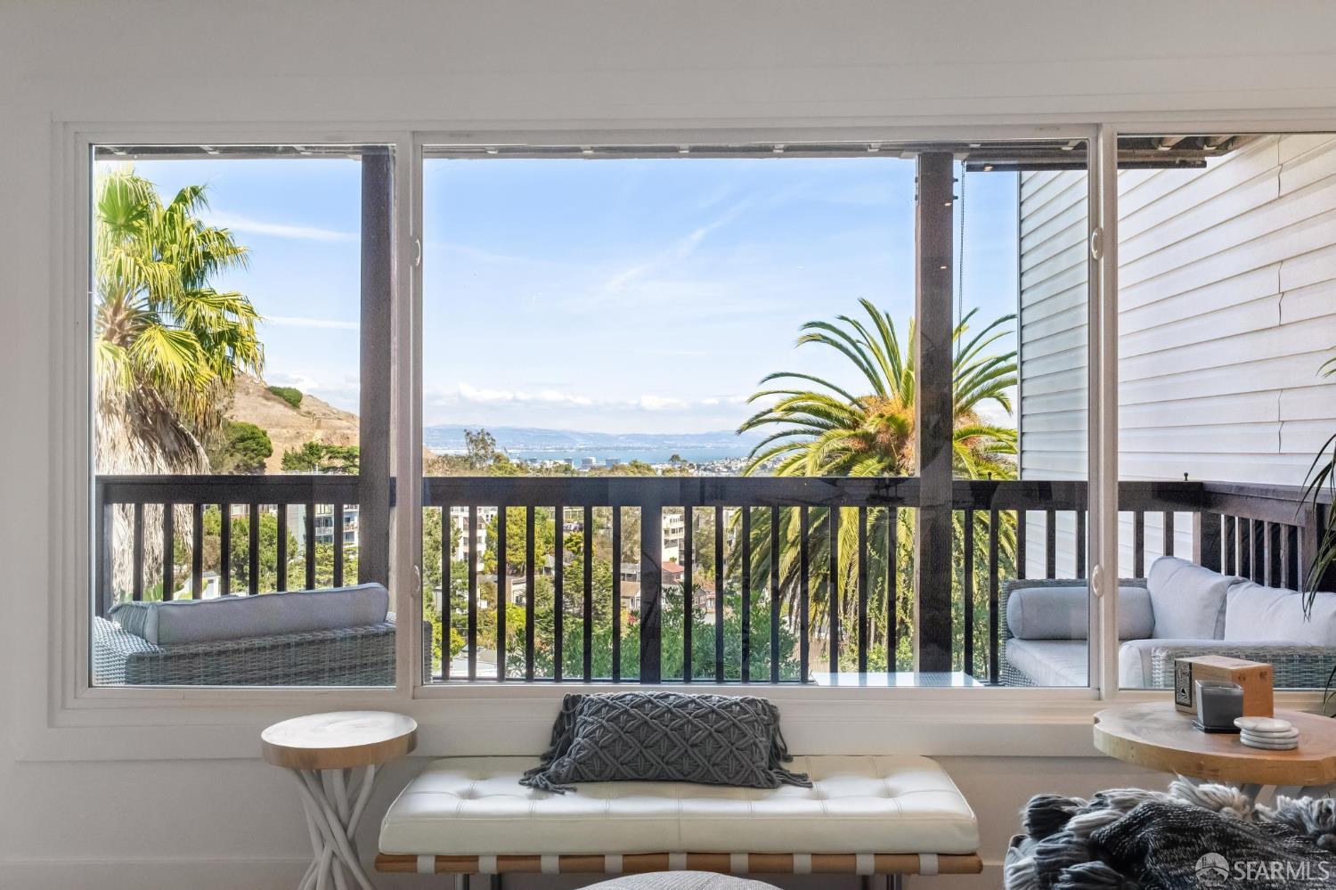 Living area with wide glass doors framing a palm-lined balcony and bay view.