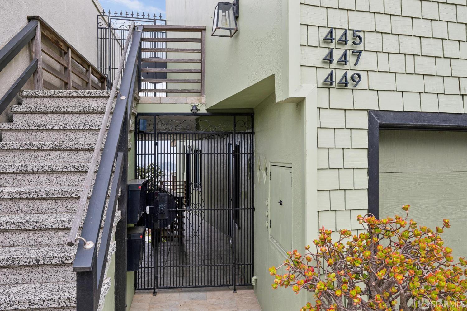 Multi-unit building entrance with exterior stairs, a security gate, and numbered siding.