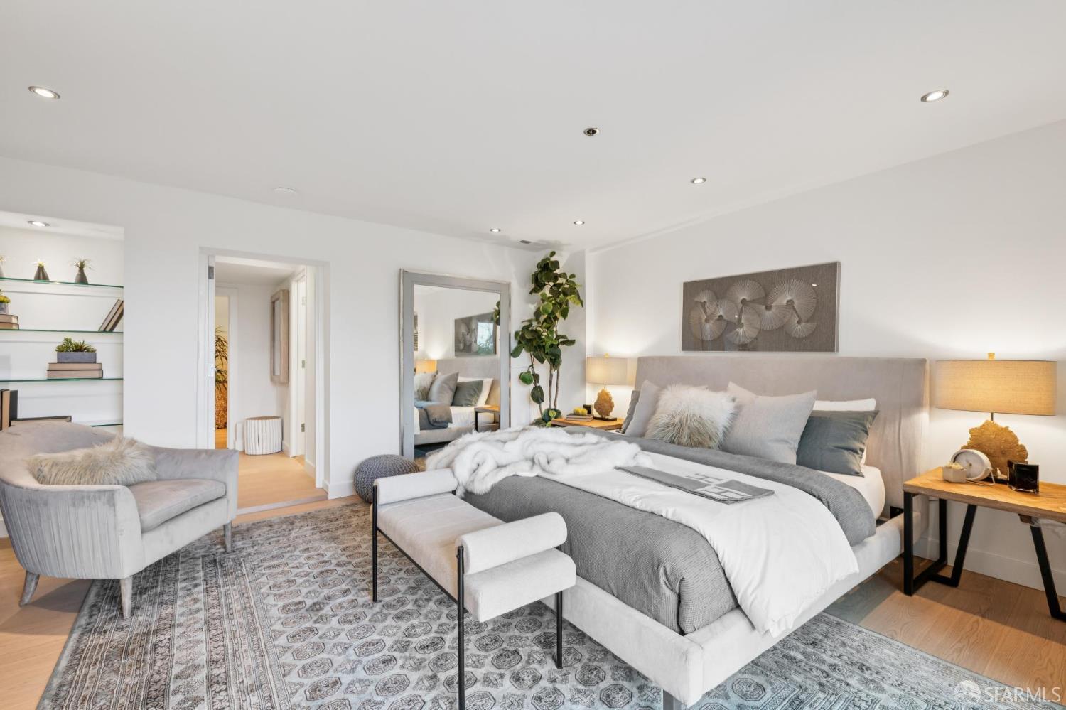 Staged bedroom with a gray upholstered bed, patterned rug, and cushioned chair.