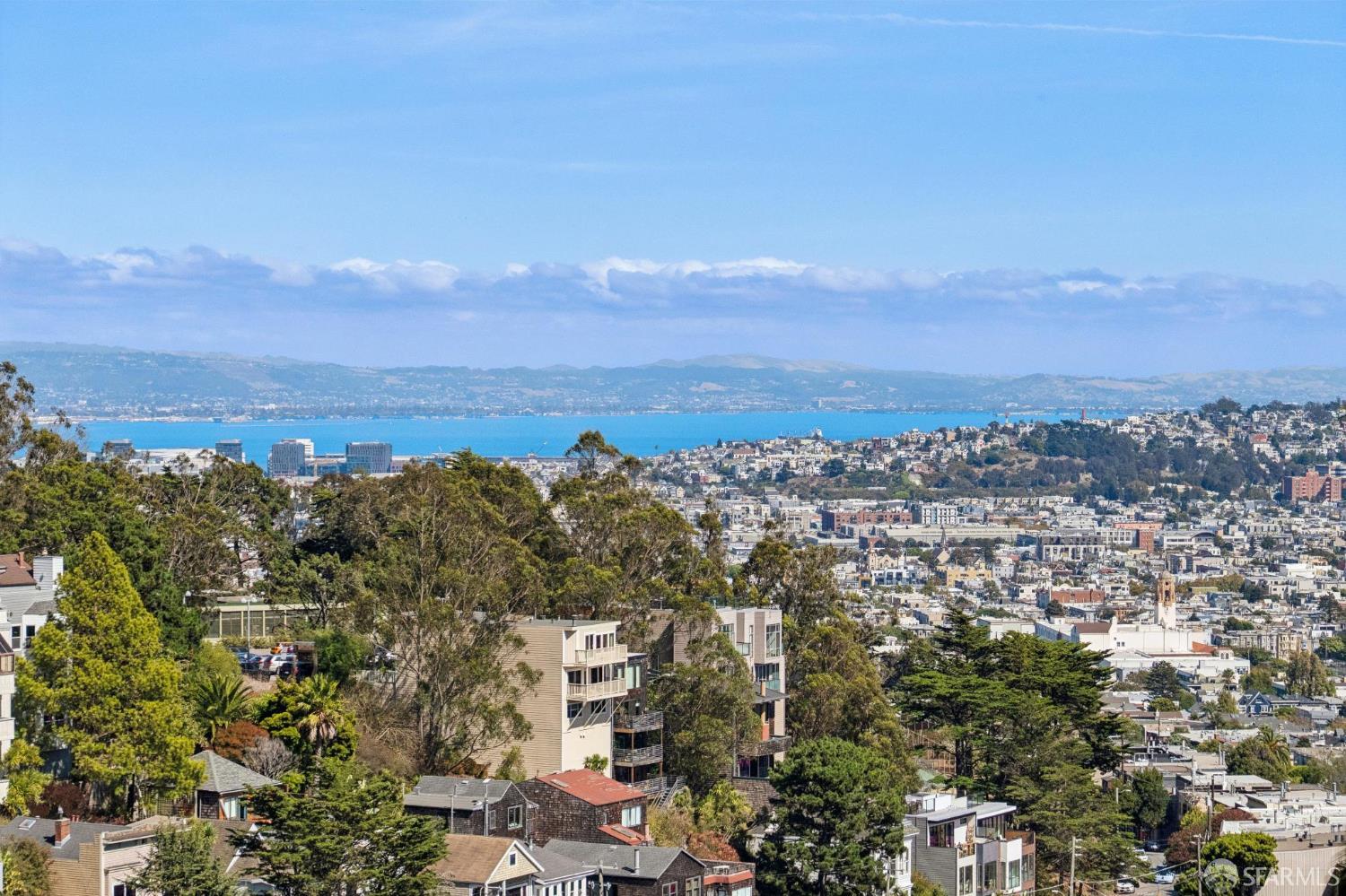 San Francisco Bay view over hillside homes and trees, with distant hills across the water.