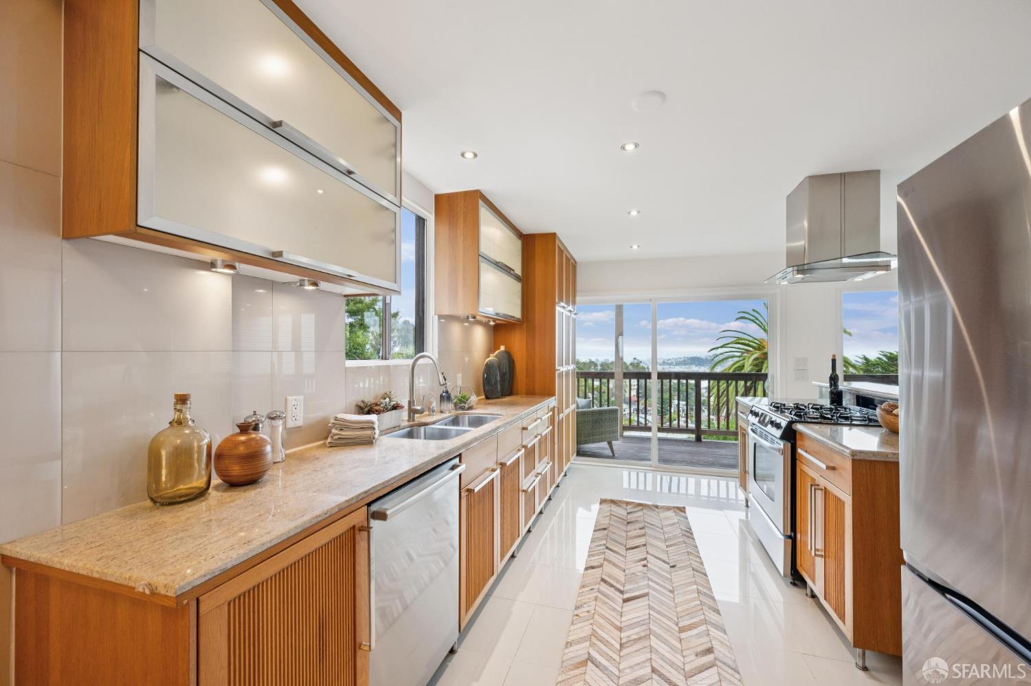 Galley kitchen with warm wood cabinets, stainless appliances, and sliding doors to a leafy balcony.