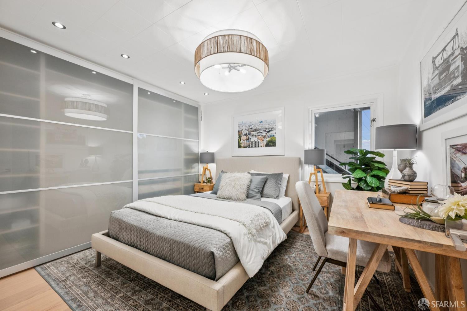Staged bedroom with a beige upholstered bed, frosted sliding closet doors, and a wooden desk.