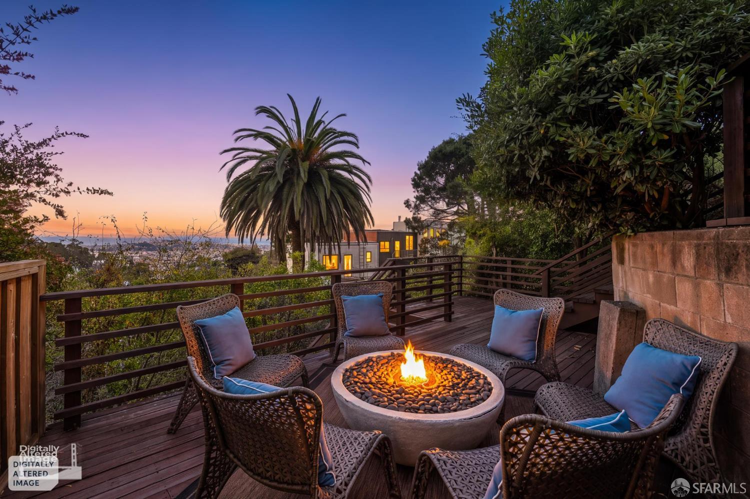 Furnished outdoor deck with a fire pit, wicker seating, and distant city views at dusk.