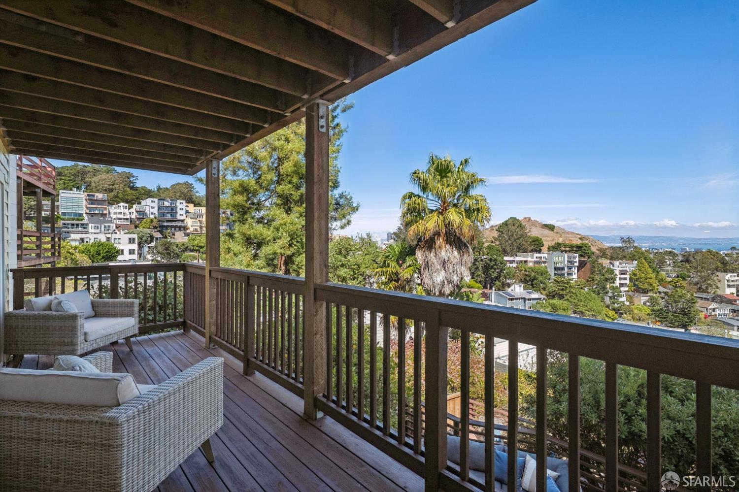 Covered deck with wicker seating and views of hillside homes and the bay.