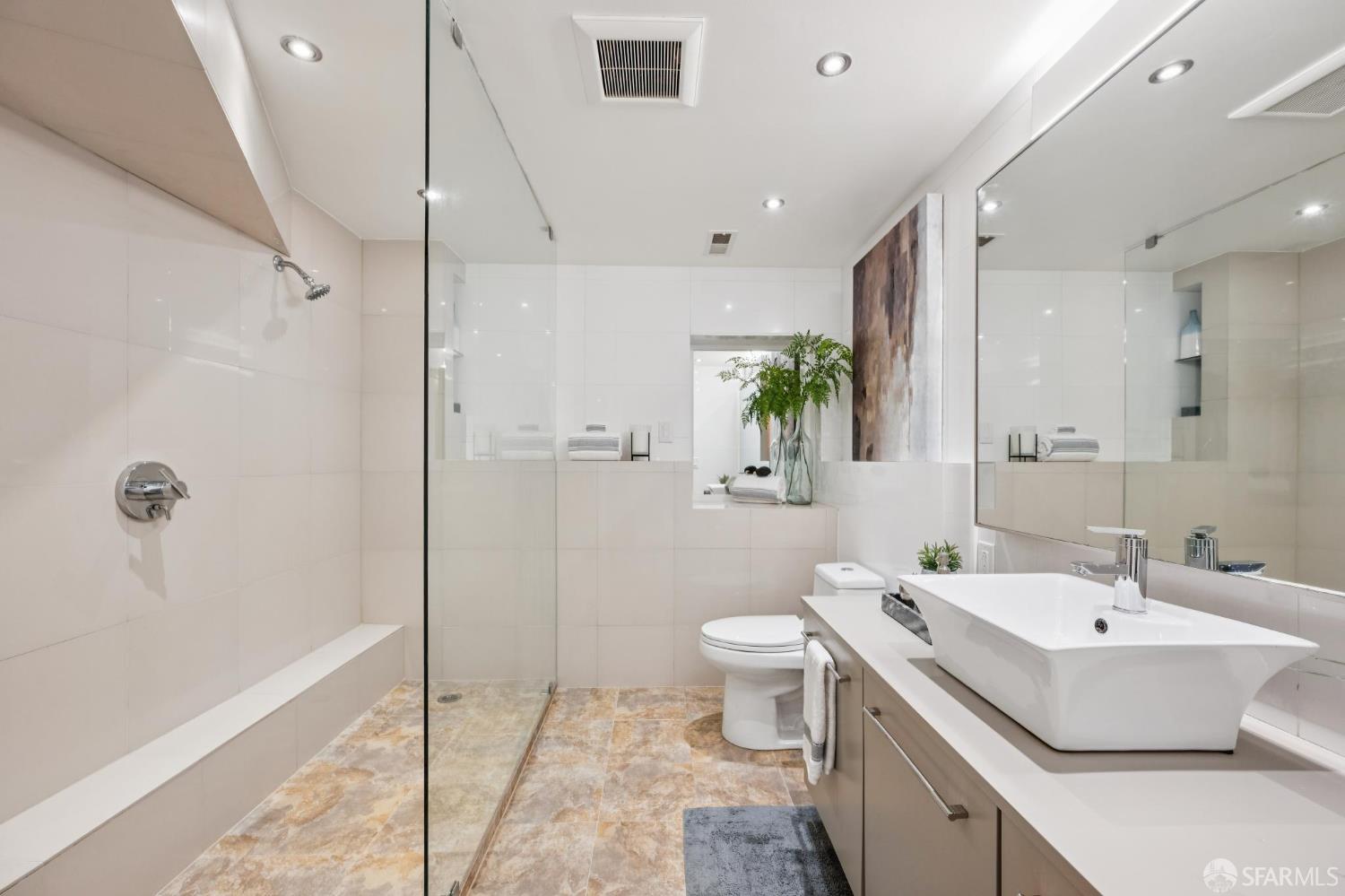 Bright bathroom with a glass walk-in shower, vessel sink, and warm-toned tile floor.