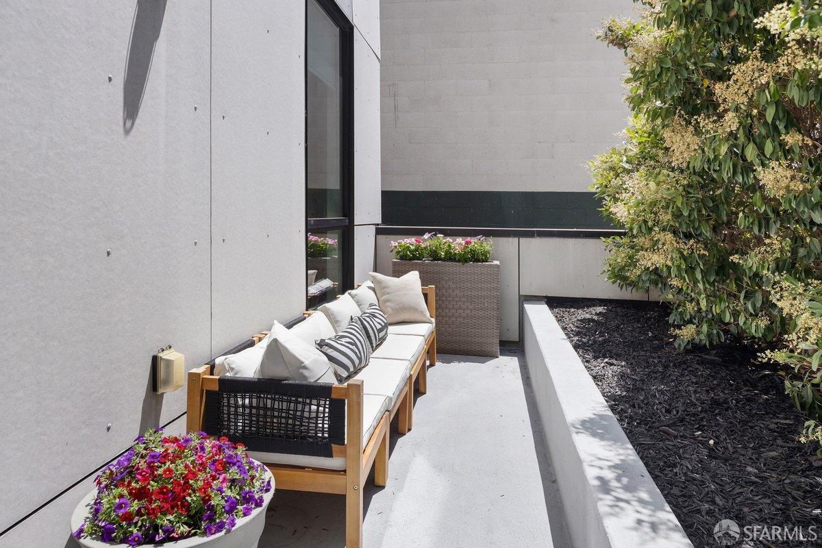 Private patio with a cushioned outdoor sofa, colorful flowers, and a raised garden bed.