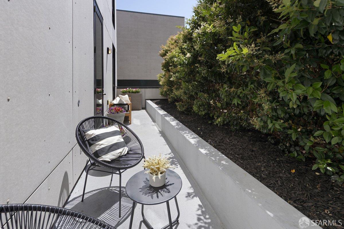 Modern patio with black wire chairs, a small table, potted flowers, and a long leafy planter.