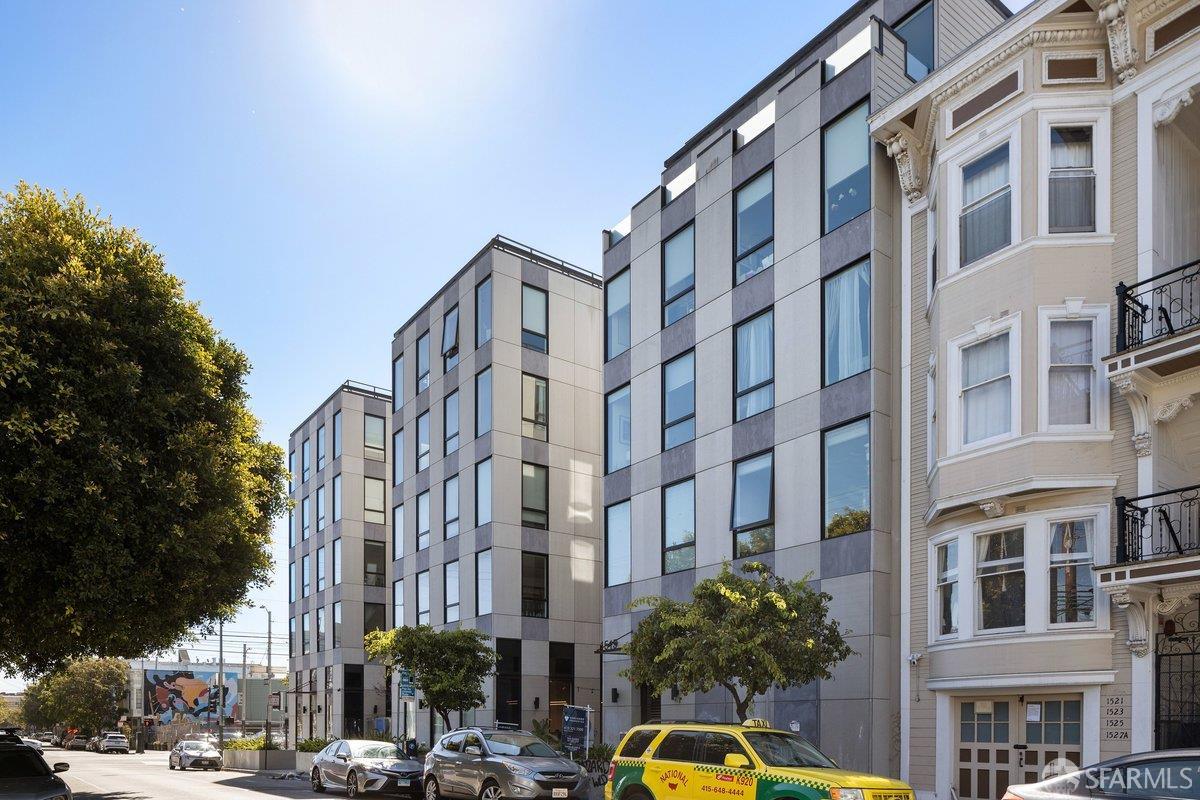 Modern gray apartment building with large windows beside an ornate Victorian on a sunny city street.