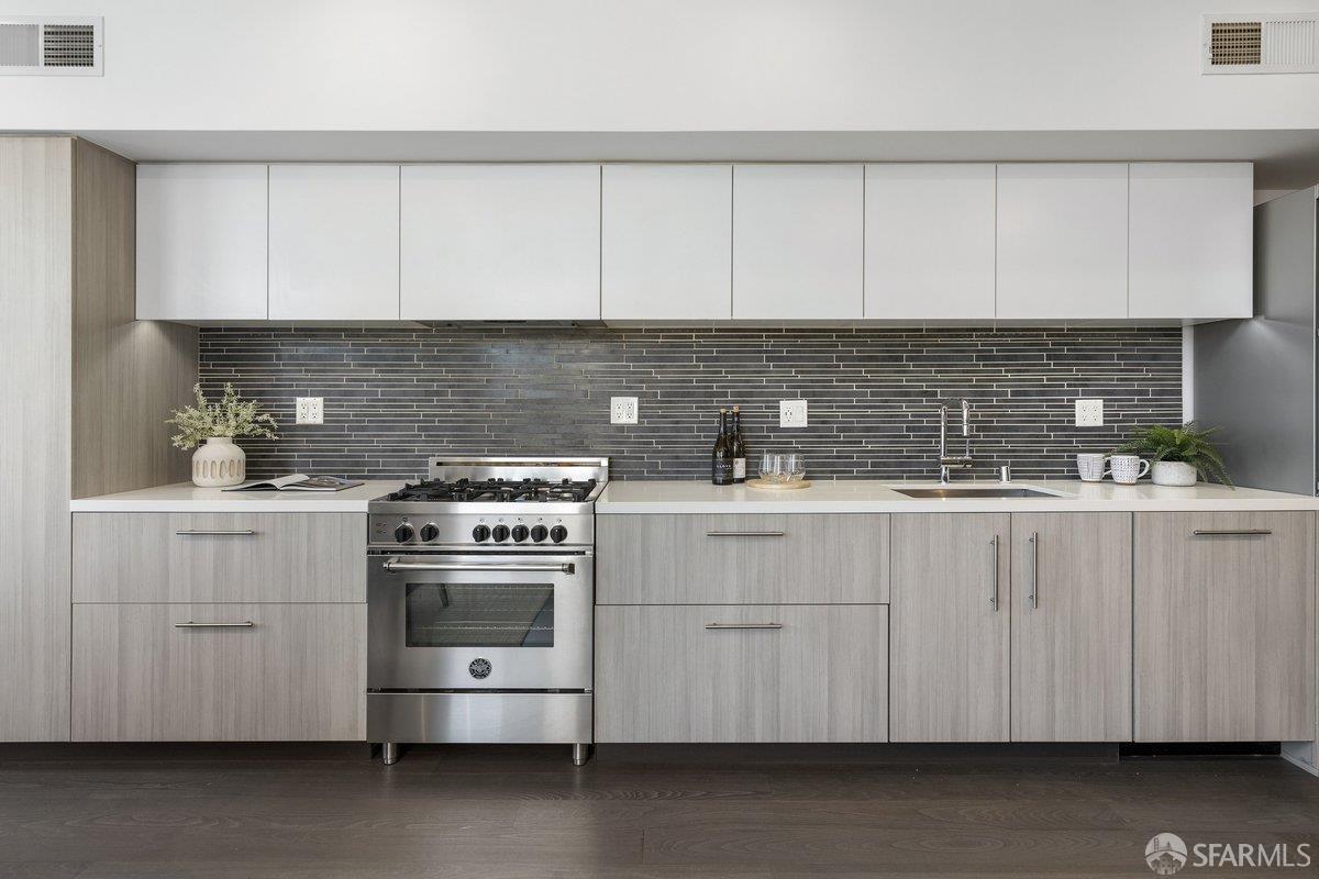 Modern kitchen with light gray cabinetry, dark tile backsplash, and stainless steel gas range.