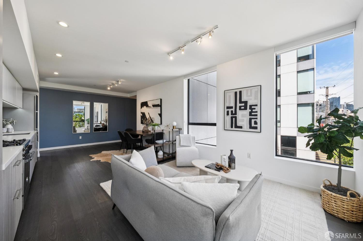 Open-plan living room with a gray sofa, dining area, dark floors, and large city-facing windows.