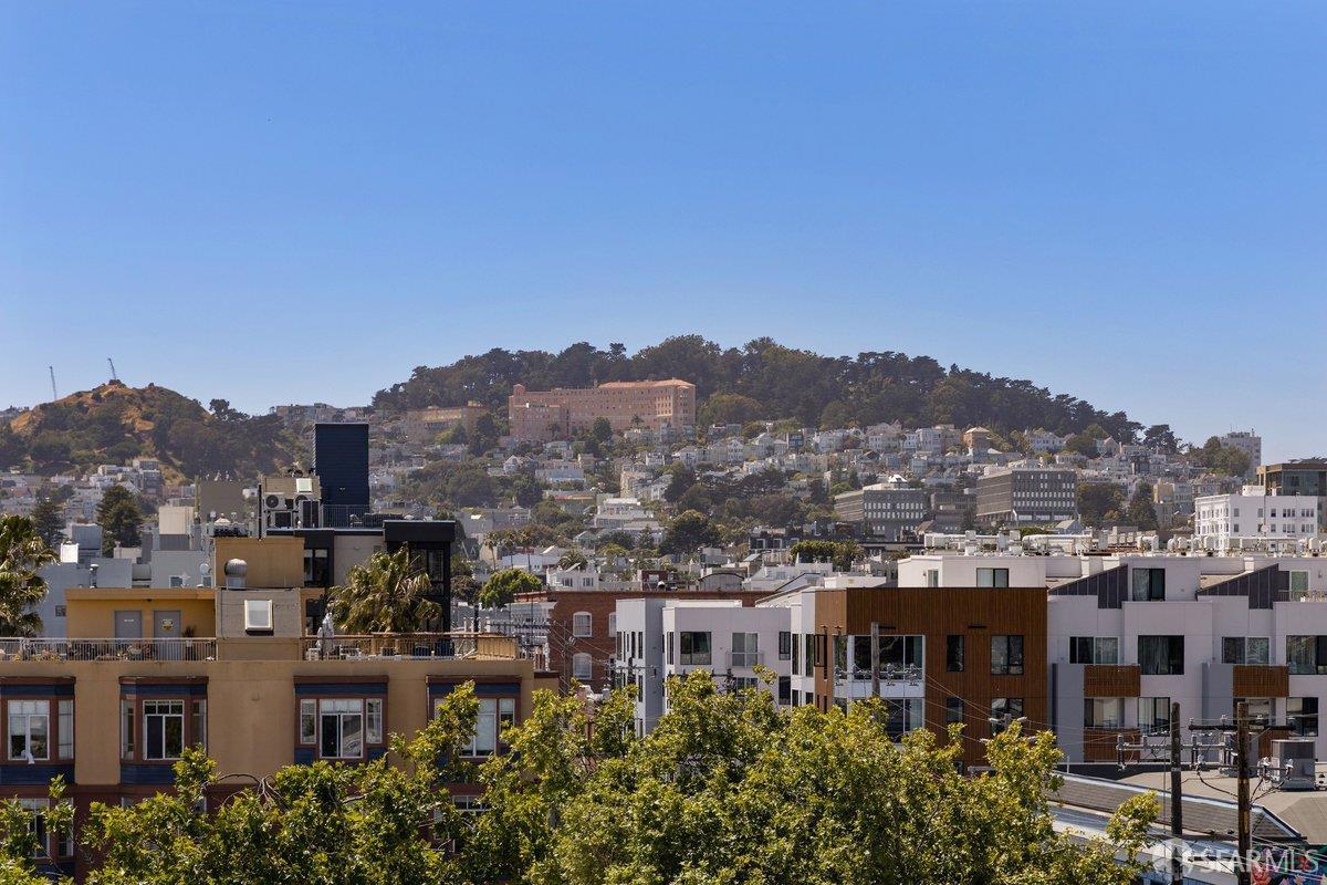 San Francisco rooftops and tree-covered hillside beneath a clear blue sky.