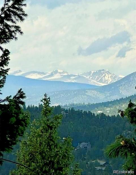 Snow-capped Rocky Mountains rise beyond forested hills, with homes visible below.