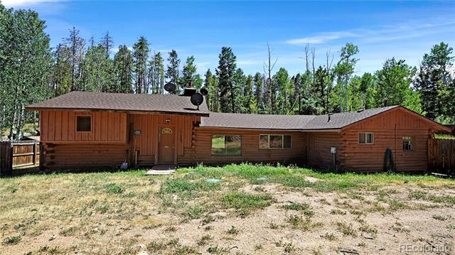 Wood-and-log house with a dry yard and tall trees behind it.